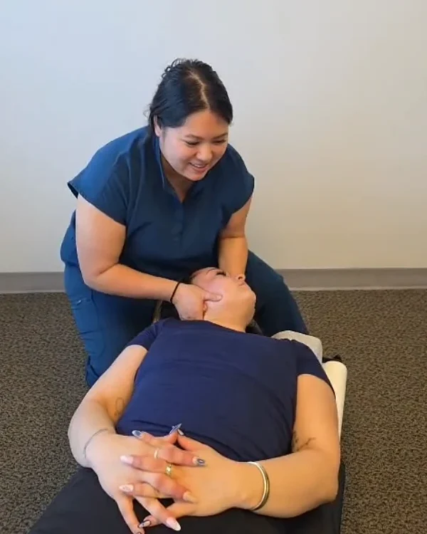 A chiropractor smiling as she treats a patient’s neck